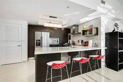 a dinning room with stainless steel appliances kitchen island granite countertop a refrigerator a stove a microwave oven with white cabinets and chairs