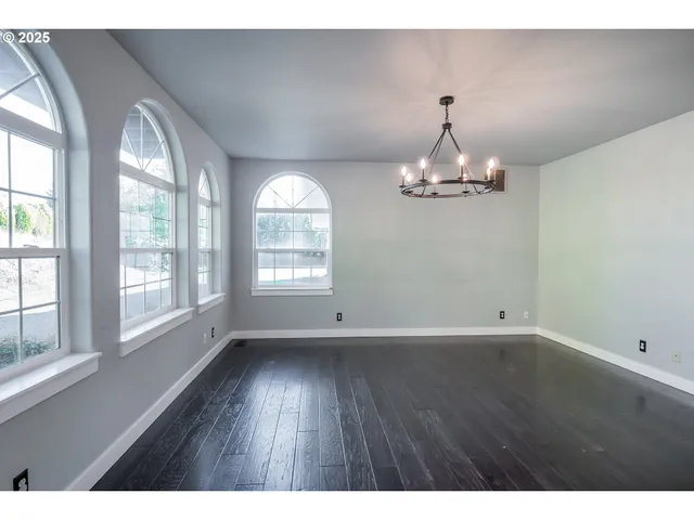 an empty room with wooden floor chandelier and windows