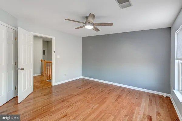 an empty room with wooden floor a ceiling fan and windows