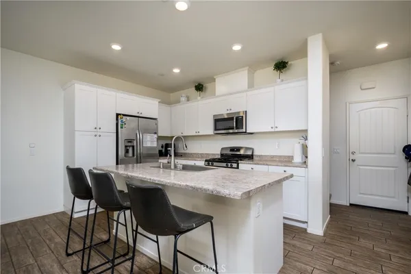 a white kitchen with stainless steel appliances granite countertop a stove a refrigerator a sink dishwasher and white cabinets with wooden floor