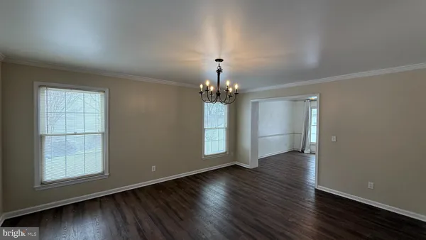 an empty room with wooden floor chandelier and windows