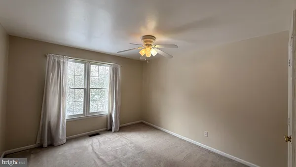 an empty room with chandelier fan and windows
