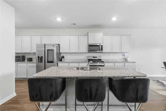 a kitchen with stainless steel appliances granite countertop a stove a sink a microwave a refrigerator and white cabinets