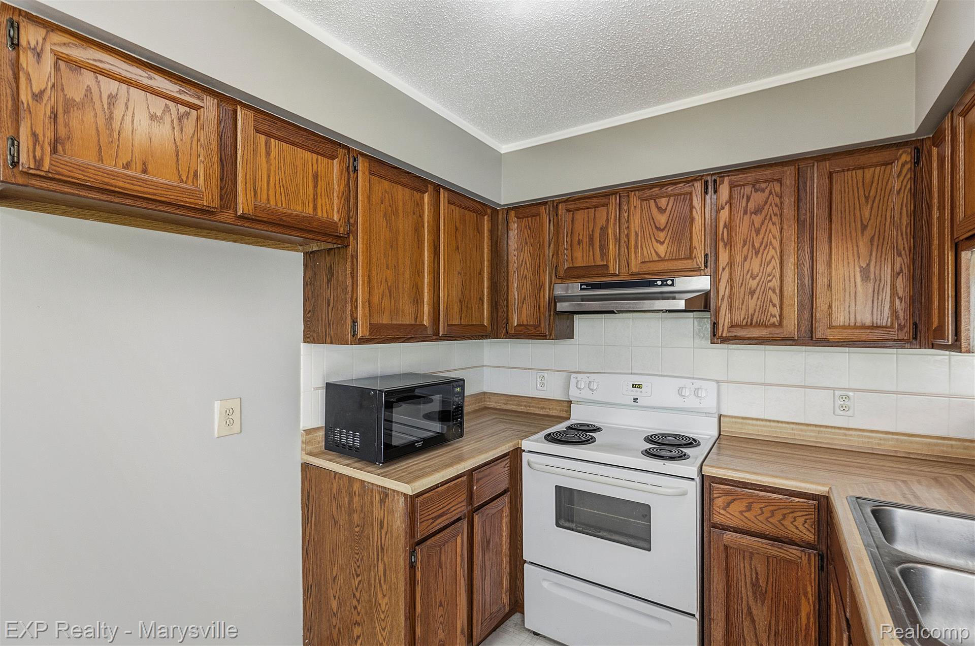 12265 Hough Road Memphis, MI 48041 - Photo 12 of 41 Kitchen featuring white range with electric stovetop, light countertops, wood finish cabinetry, tasteful backsplash, and a textured ceiling