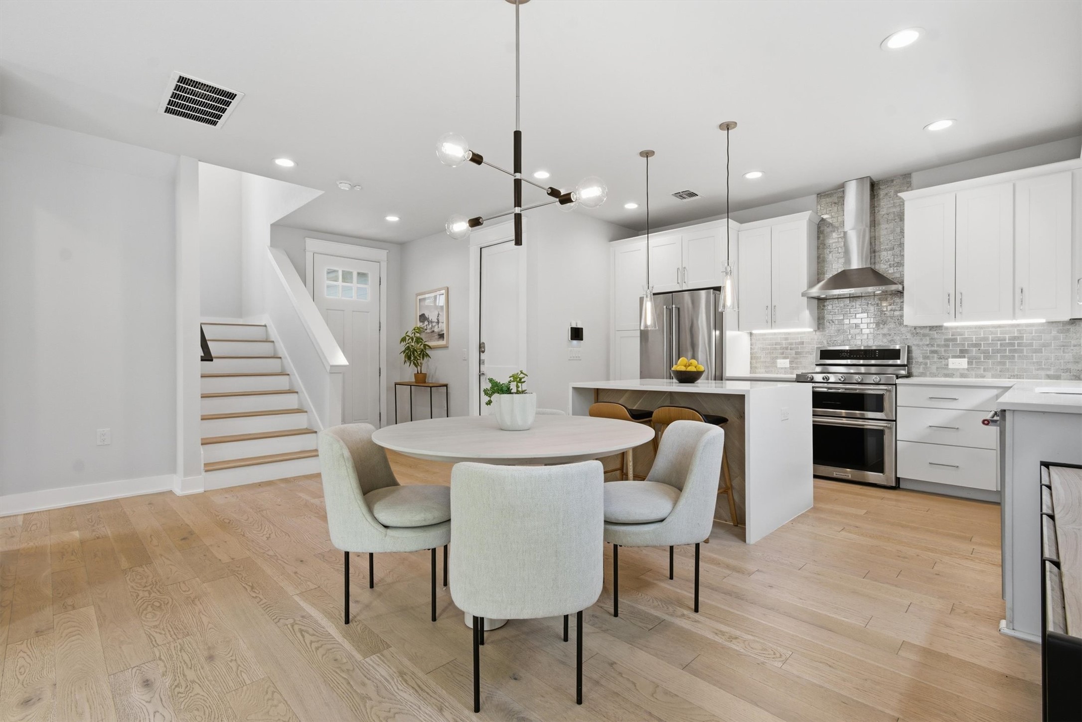2710 Zaragosa Street, Unit A Austin, TX 78702 - Photo 11 of 29 Open kitchen and dining flow with island seating, stainless appliances, and a dramatic staircase backdrop — built for entertaining.