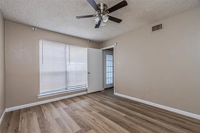 an empty room with wooden floor fan and windows