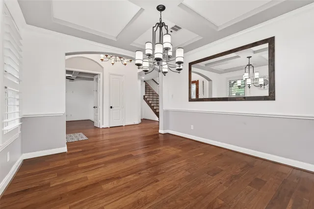 an empty room with wooden floor chandelier and entryway