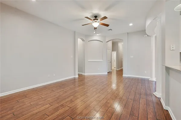a view of an empty room with wooden floor and a ceiling fan
