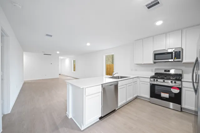 a kitchen with stainless steel appliances granite countertop a stove top oven a sink dishwasher and a refrigerator with wooden floor