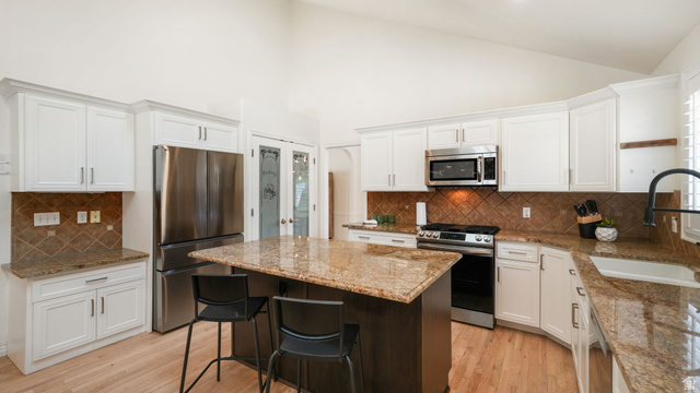 11128 South Barrett Pk Circle Sandy, UT 84092 - Photo 9 of 36 Kitchen featuring white cabinetry, stainless steel appliances, a central island with countertop seating, granite countertops, and a tiled backsplash
