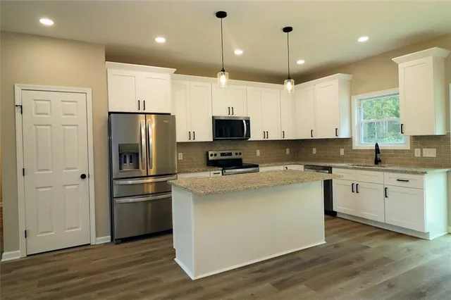 a kitchen with stainless steel appliances granite countertop a refrigerator a stove a sink and white cabinets with wooden floor