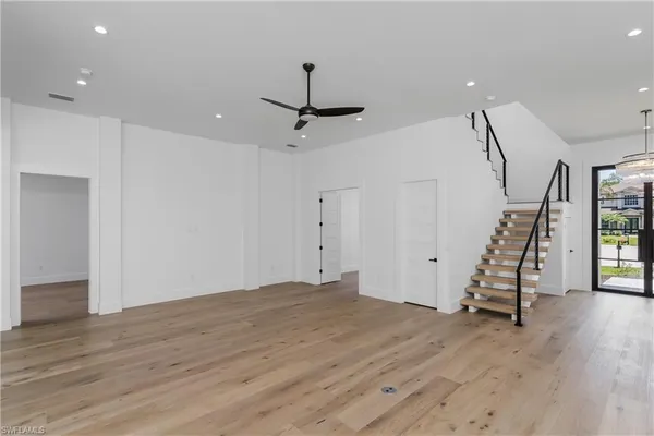 a view of an empty room with wooden floor stairs and a chandelier