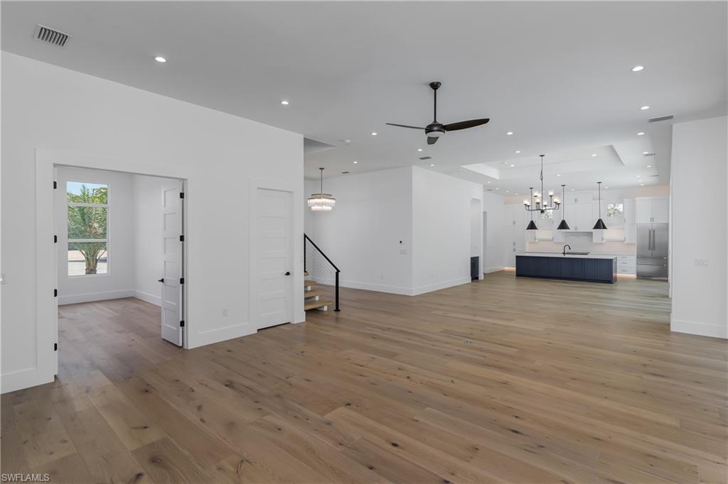 2854 Coach House Way Naples, FL 34105 - Photo 9 of 50 Unfurnished living room with a tray ceiling, light wood finished floors, a chandelier, a ceiling fan, and recessed lighting