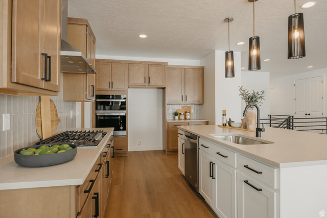 1066n South State Road, Unit ATWOOD Salem, UT 84653 - Photo 20 of 29 Open-concept kitchen featuring wood-finish flooring, light wood cabinetry, a stainless steel range hood, and a kitchen island with a built-in sink and pendant lighting