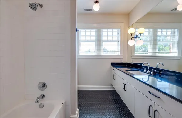 a bathroom with a granite countertop sink mirror bathtub and next to a window