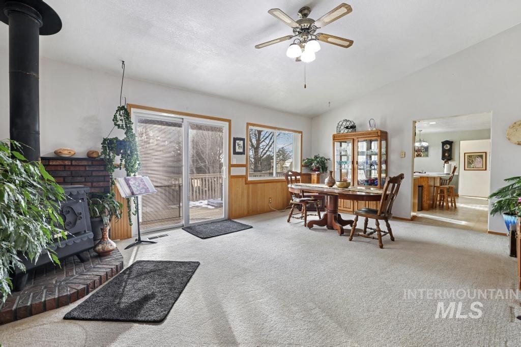 213 Sage Road West Jerome, ID 83338 - Photo 25 of 50 familoy/Dining room combo featuring a wood stove, carpet, vaulted ceiling, and a ceiling fan