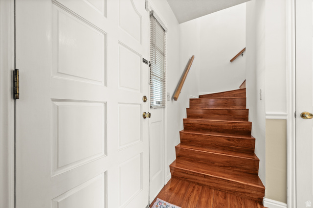 1650 Nichole Circle Sandy, UT 84093 - Photo 12 of 31 Wood-finish staircase with a natural wood handrail, white paneled walls, and a white paneled door with brass hardware