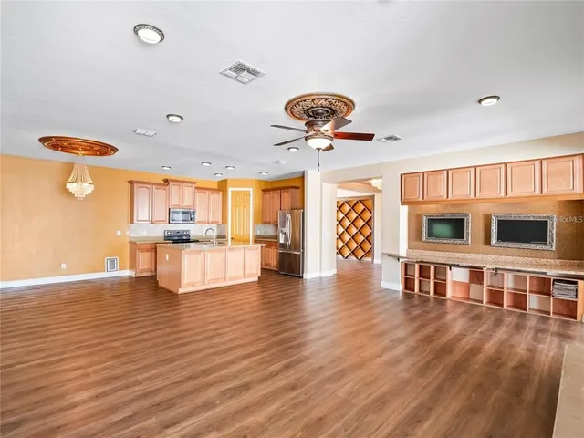 a view of an empty room and kitchen with wooden floor
