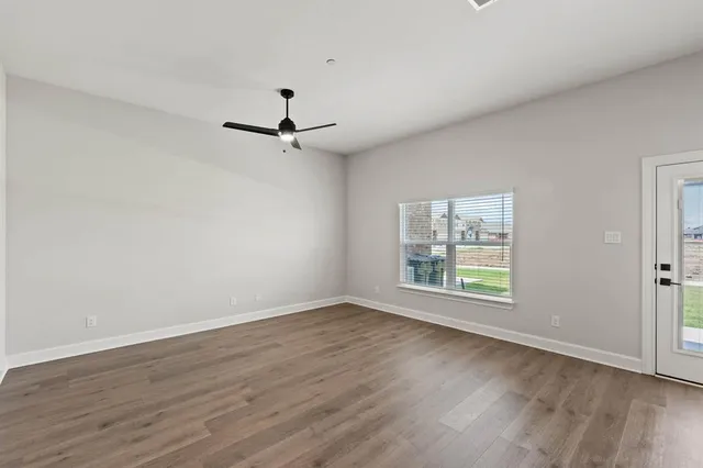 an empty room with wooden floor fan and windows