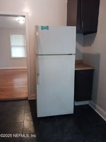 a view of a refrigerator in kitchen and an empty room