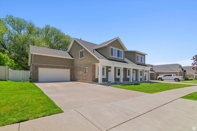 847 225 South Springville, UT 84663 - Photo 21 of 23 Exterior featuring a brick and stucco facade, a prominent two-car garage, a covered front porch with white columns, and a well-maintained front lawn