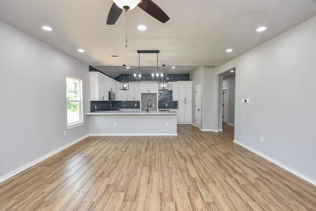 an empty room with wooden floor kitchen view and a window