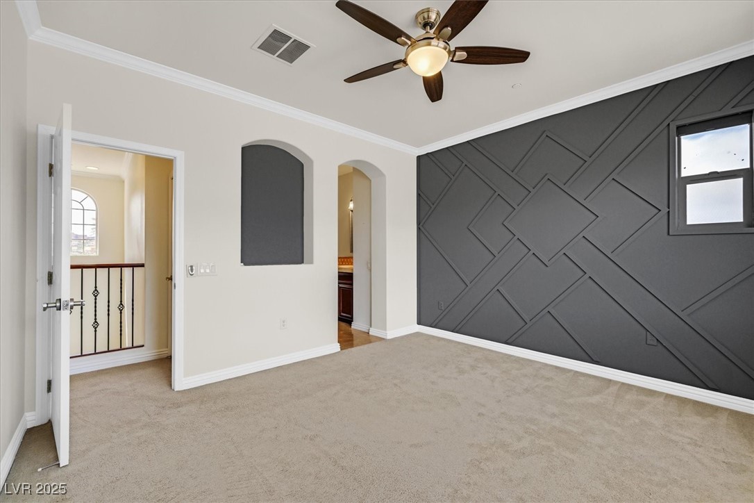 31 Via Mantova, Unit 2 Henderson, NV 89011 - Photo 11 of 30 Unfurnished room featuring ornamental molding, an accent wall, a ceiling fan, arched walkways, and light carpet