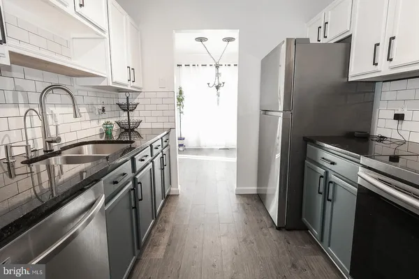 a kitchen with stainless steel appliances a sink dishwasher a refrigerator and a stove with wooden floor
