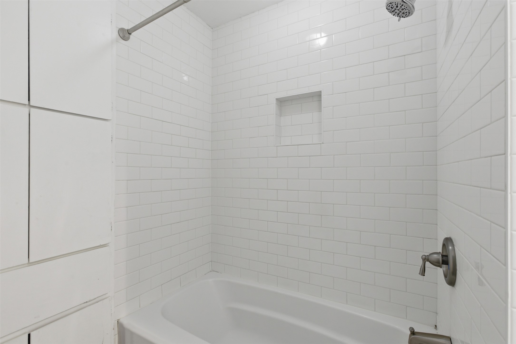 4204 Hudson Bend Road, Unit B Austin, TX 78734 - Photo 19 of 37 Bathtub and shower combination featuring white subway tile surround, built-in recessed shelf, brushed nickel showerhead, and matching plumbing fixtures