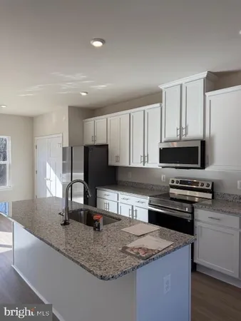 a kitchen with granite countertop a sink a stove top oven a counter space and cabinets
