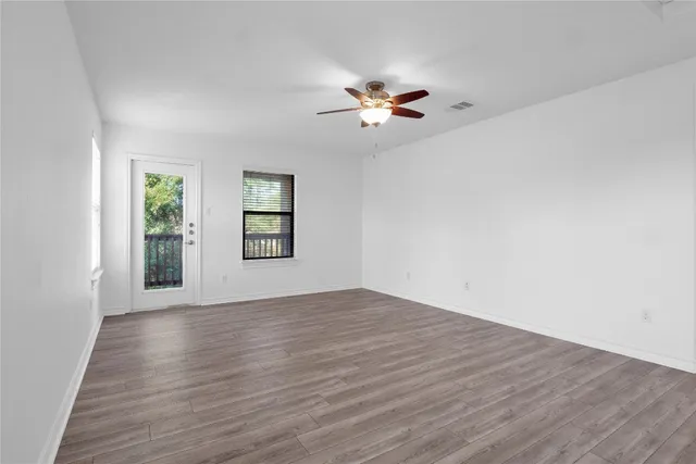 an empty room with wooden floor chandelier fan and windows