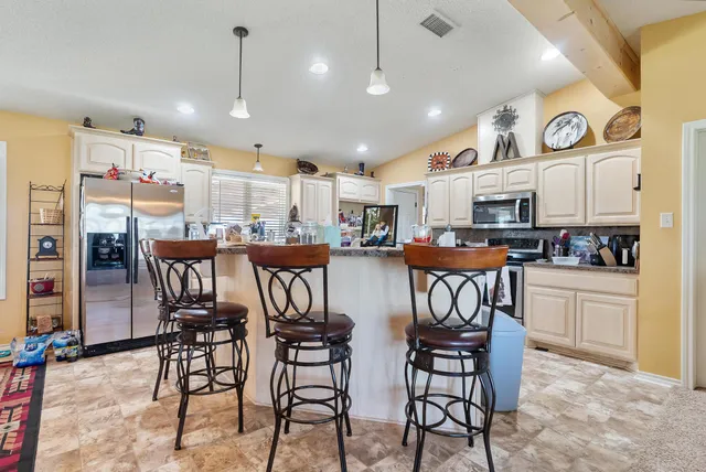 a kitchen with stainless steel appliances kitchen island granite countertop a refrigerator a stove a dining table and chairs with wooden floor
