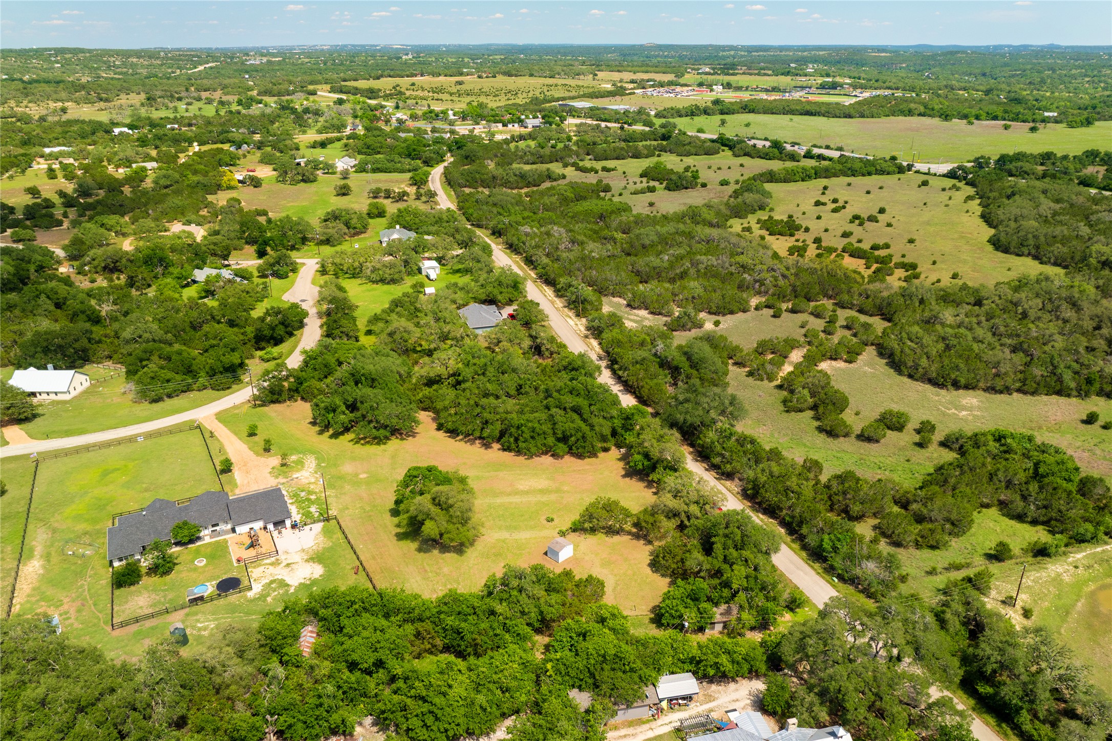 187 Beauchamp Road Dripping Springs, TX 78620 - Photo 15 of 19 Expansive rural landscape featuring a single-story residence with a dark-pitched roof, surrounded by green lawns and mature trees