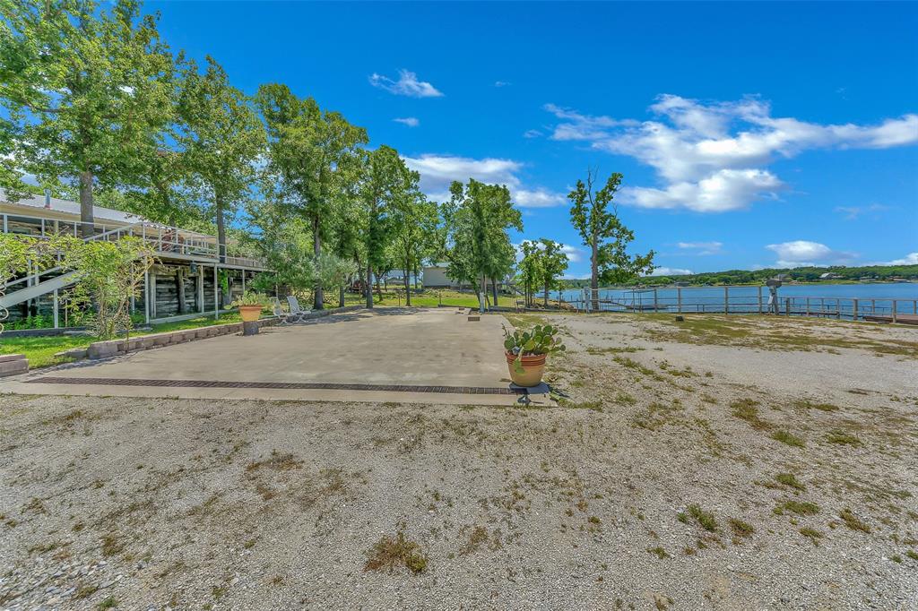 566 Selma Park Road Bowie, TX 76230 - Photo 26 of 40 Waterfront property featuring a gravel lot, concrete pad, mature trees, and a multi-level deck structure