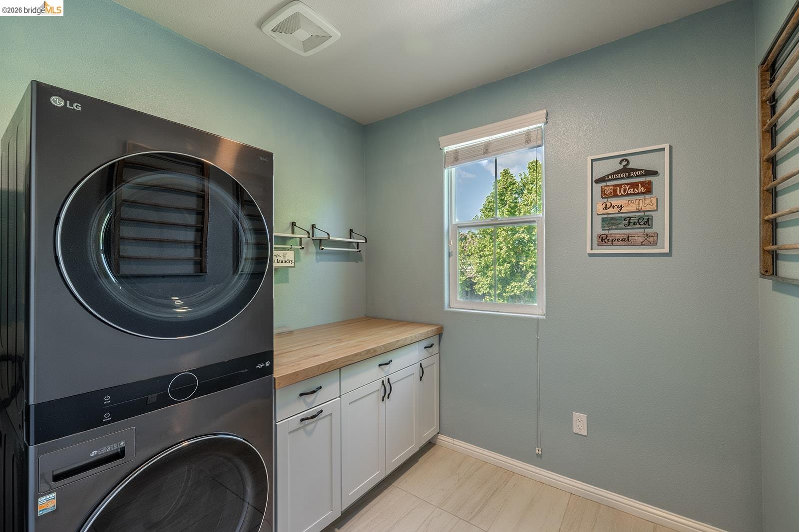 974 Princess Way Brentwood, CA 94513 - Photo 32 of 49 Dedicated laundry area featuring a stacked washer and dryer, wood-finish countertop, white base cabinetry with dark hardware, and a single window
