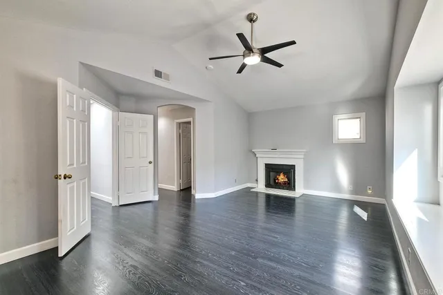 a view of a livingroom with a fireplace a ceiling fan and windows