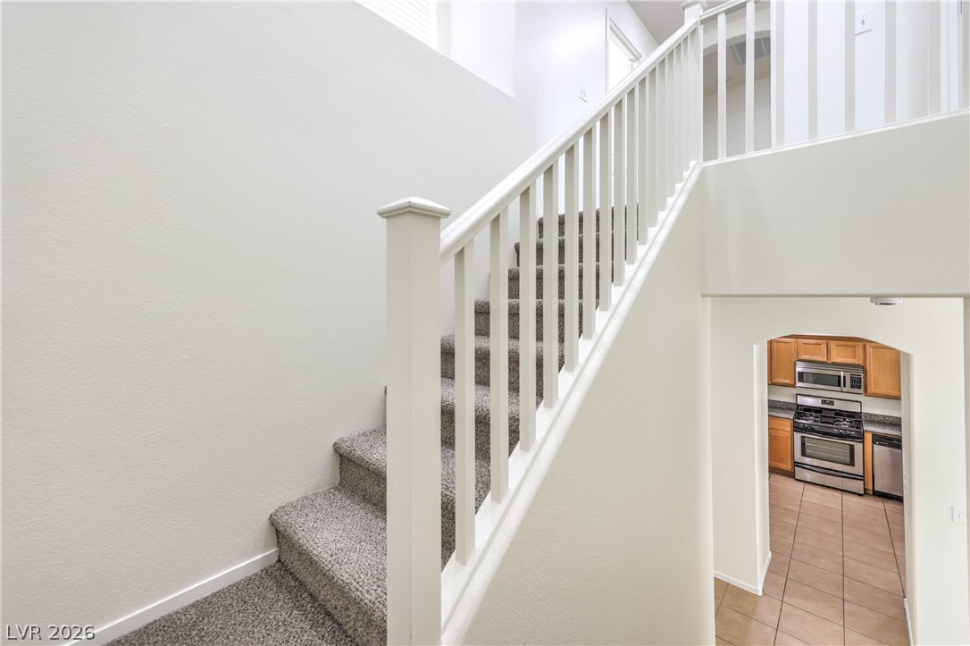 10939 Paradise Road Henderson, NV 89052 - Photo 18 of 36 A carpeted staircase with a crisp white railing ascends, offering a peek into the adjacent kitchen.