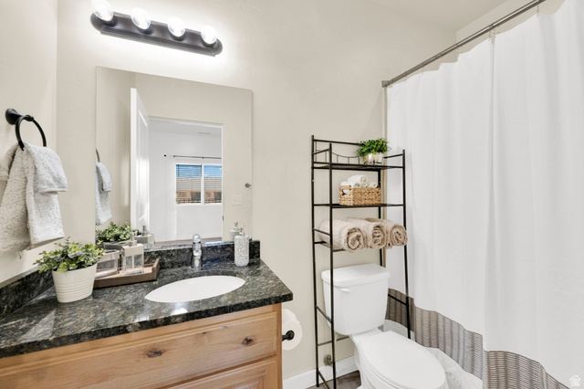8215 Clear Rock Road, Unit 12 Eagle Mountain, UT 84005 - Photo 3 of 38 Bathroom featuring a vanity with an oval sink, dark countertop, and wood-finish cabinetry