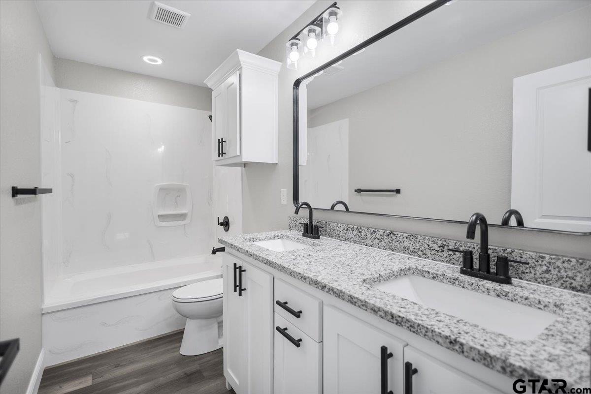 1607 North Ross Avenue Tyler, TX 75702 - Photo 28 of 39 a bathroom with a granite countertop sink a toilet a mirror and bathtub