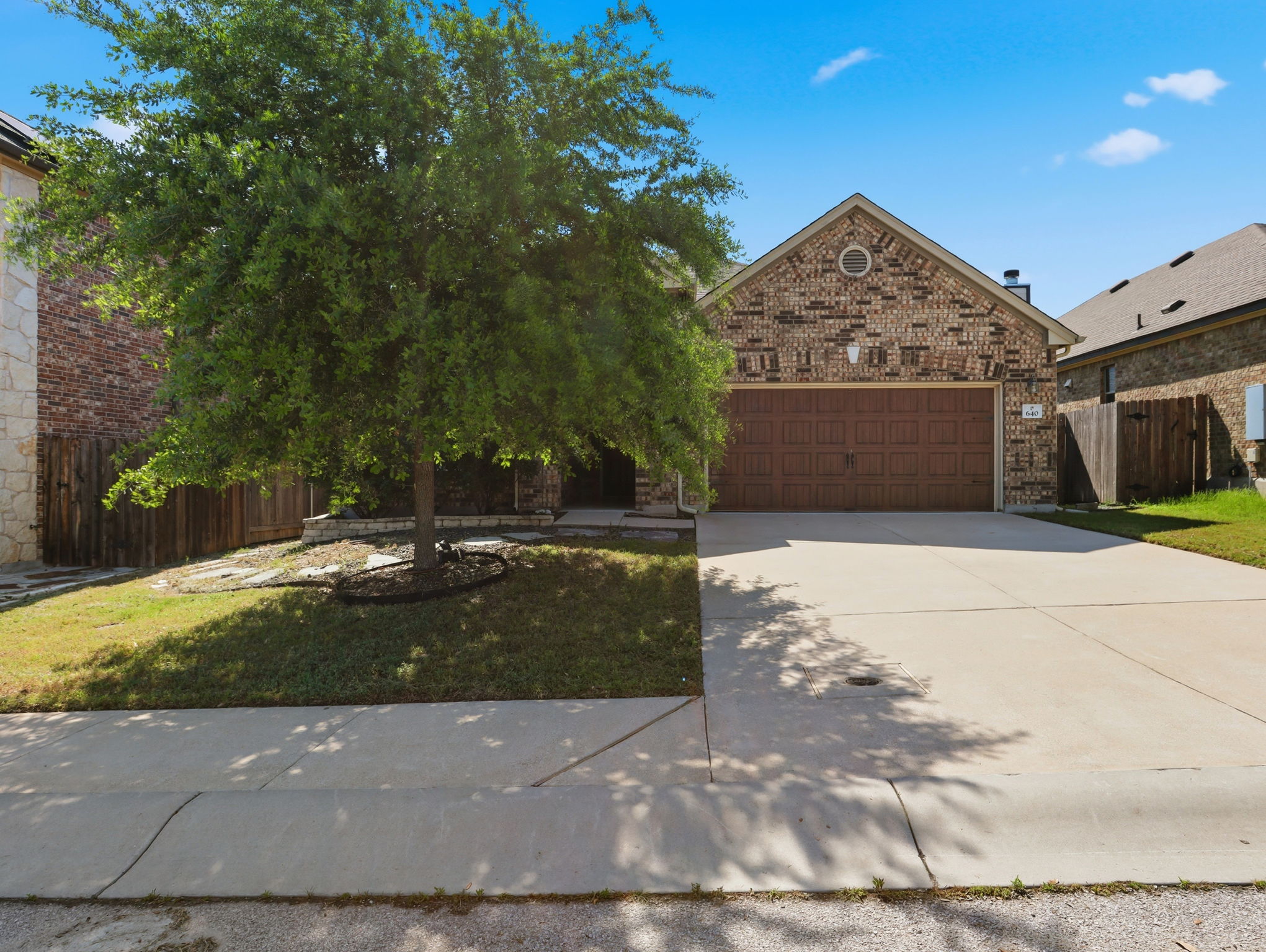640 Landon Samuel Loop Pflugerville, TX 78660 - Photo 1 of 33 Brick facade residence featuring an attached two-car garage with a brown door, a concrete driveway, a manicured front lawn, and mature tree landscaping