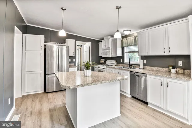 a kitchen with stainless steel appliances granite countertop a refrigerator a sink dishwasher a stove and white cabinets with wooden floor