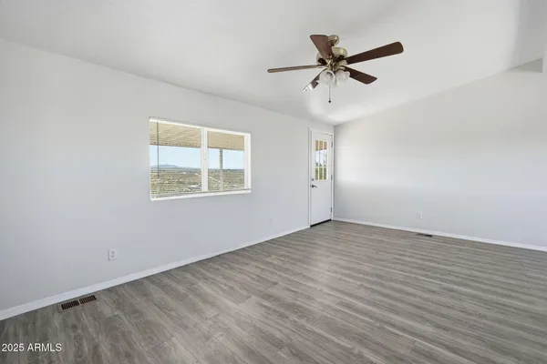 an empty room with wooden floor ceiling fan and windows