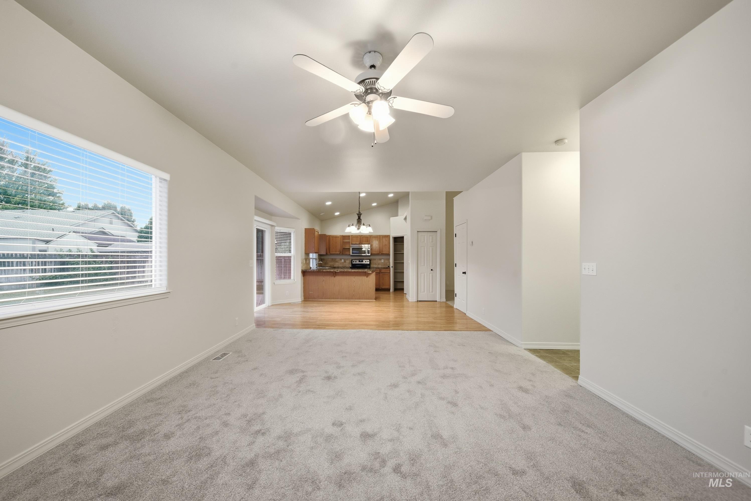 919 East Hawk Street Meridian, ID 83646 - Photo 9 of 31 Carpeted living area with a ceiling fan and large window, featuring wood-finish flooring extending into the kitchen with wood cabinetry