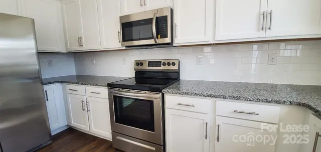 a kitchen with stainless steel appliances granite countertop white cabinets granite counter tops and a wooden floors