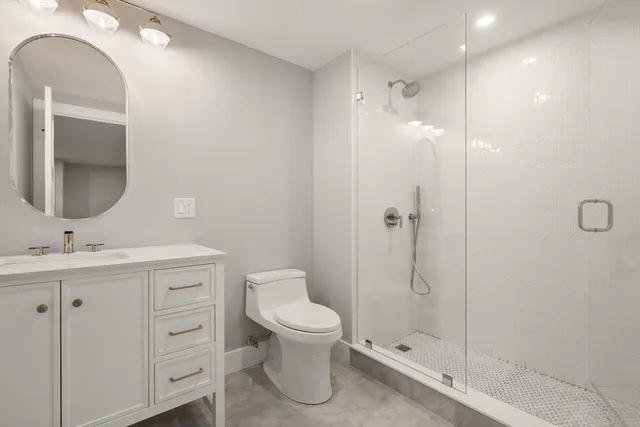 a bathroom with a toilet a sink a glass door a shower and vanity