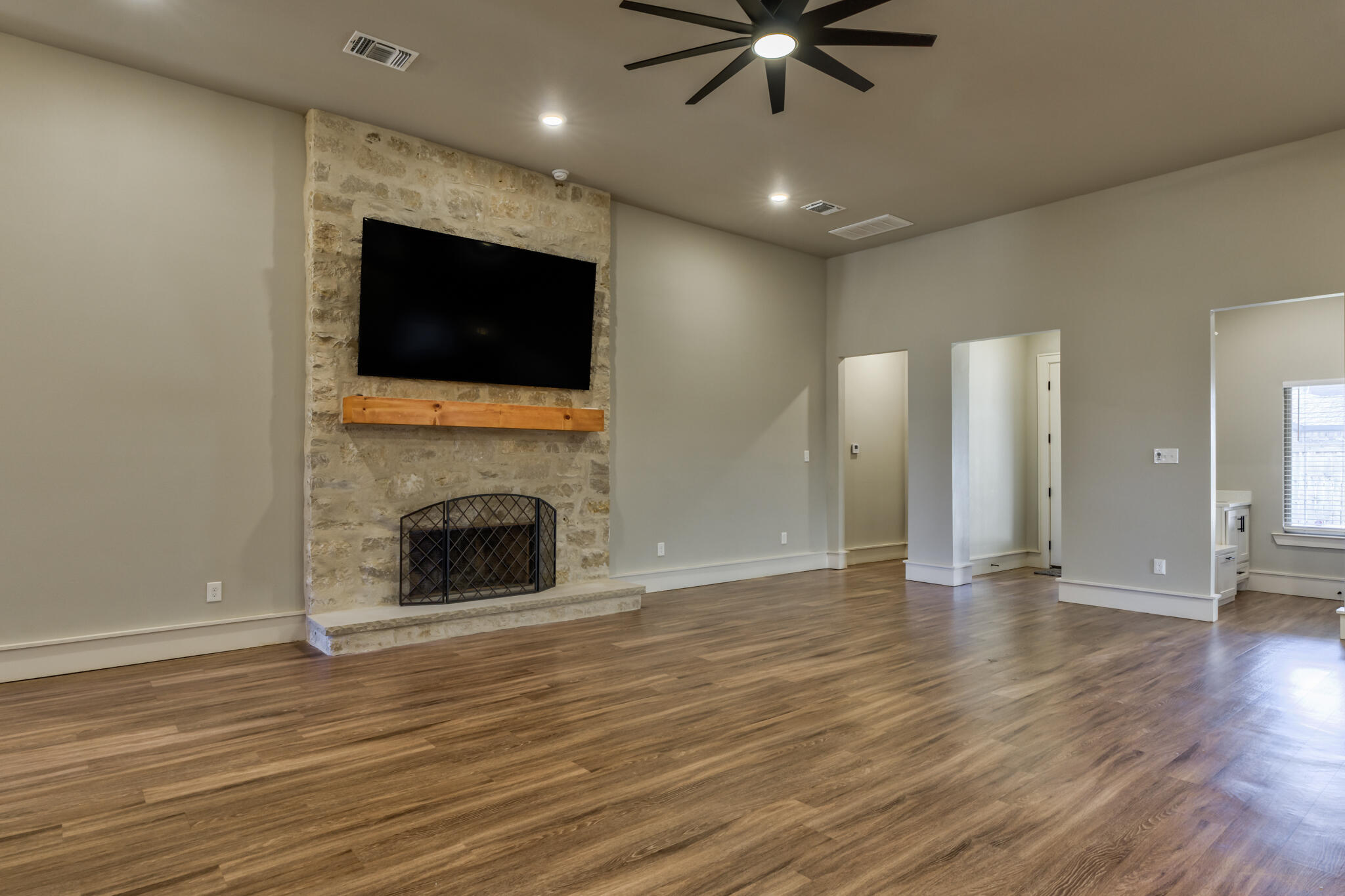 5303 110th Street Lubbock, TX 79424 - Photo 15 of 55 an empty room with wooden floor a ceiling fan a fireplace and windows
