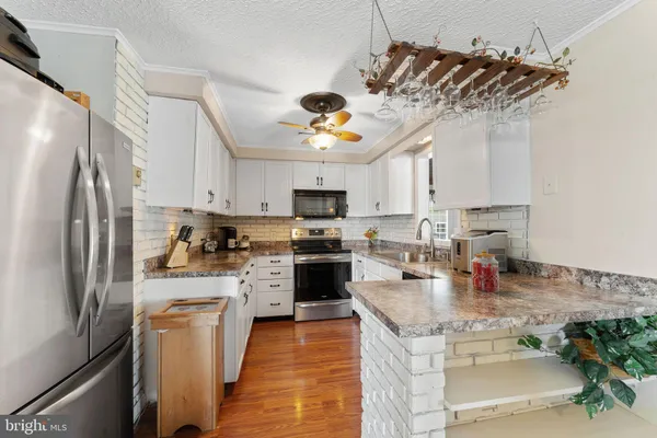 a kitchen with stainless steel appliances granite countertop a refrigerator a stove oven a sink dishwasher and white cabinets with wooden floor