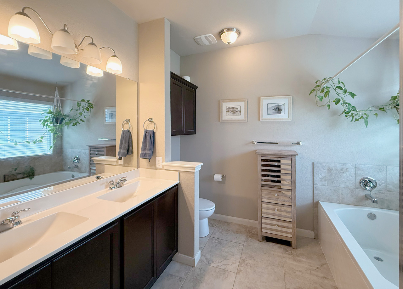 930 Pumpkin Ridge New Braunfels, TX 78130 - Photo 21 of 32 Bathroom featuring a double vanity with dark wood-finish cabinetry and integrated sinks, a built-in soaking tub with a tiled surround, a separate commode, and ceramic tile flooring