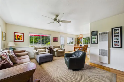 a view of a dining room and livingroom with furniture wooden floor a rug a flat screen tv a rug and a large window