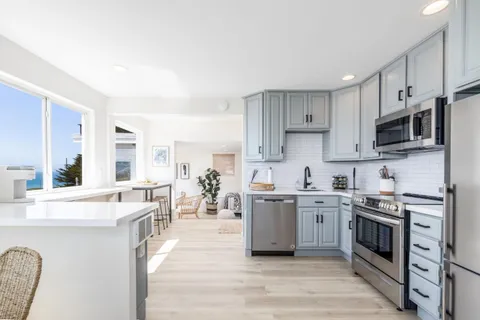 a large kitchen with stainless steel appliances granite countertop a stove top oven a sink dishwasher and white cabinets with wooden floor